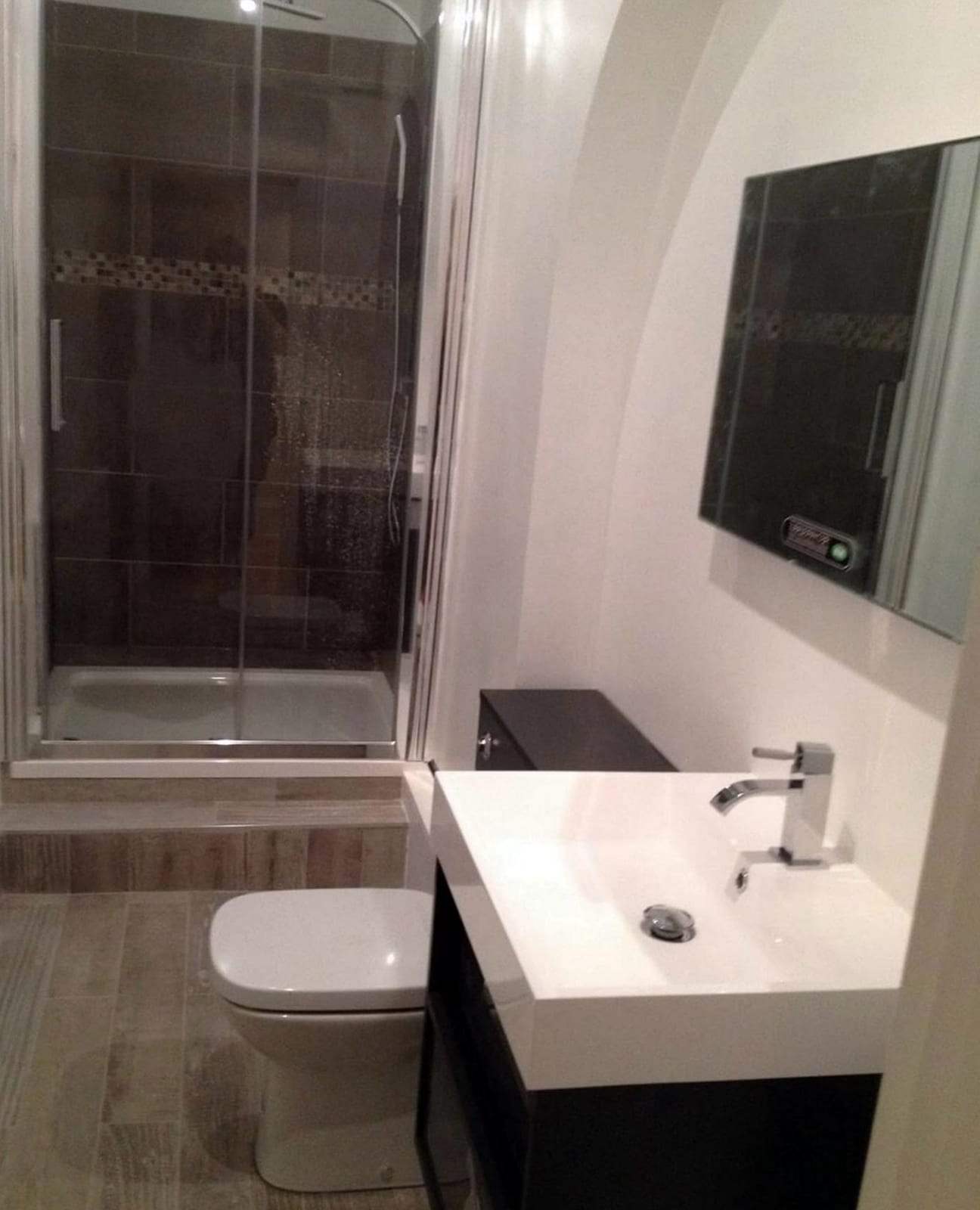 Small finished bathroom with a sliding-door shower enclosure, a white toilet and a white vanity basin with a chrome single-lever faucet on a dark cabinet