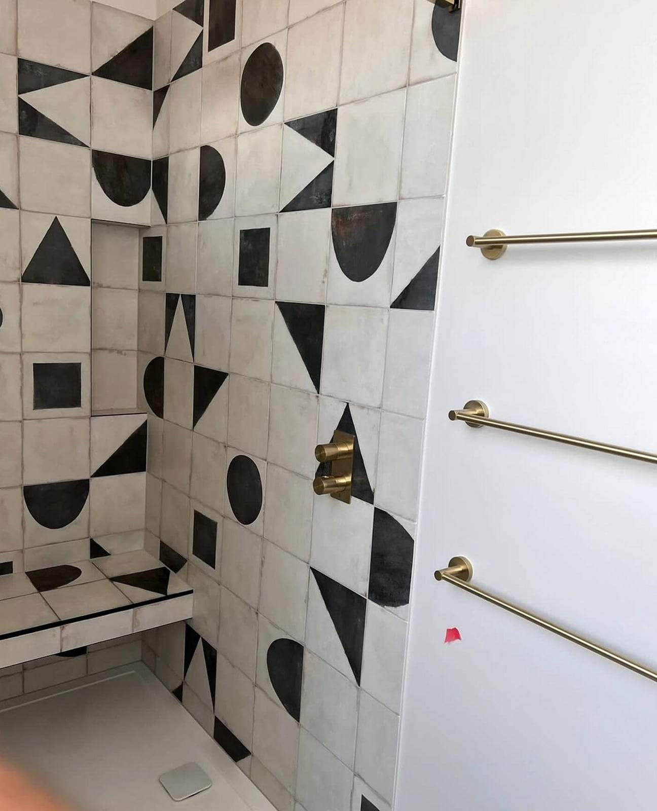 Shower walled in black-and-white geometric tile with a brushed brass thermostatic shower valve, a tiled niche and a tiled bench, brass towel bars on the white wall beside it